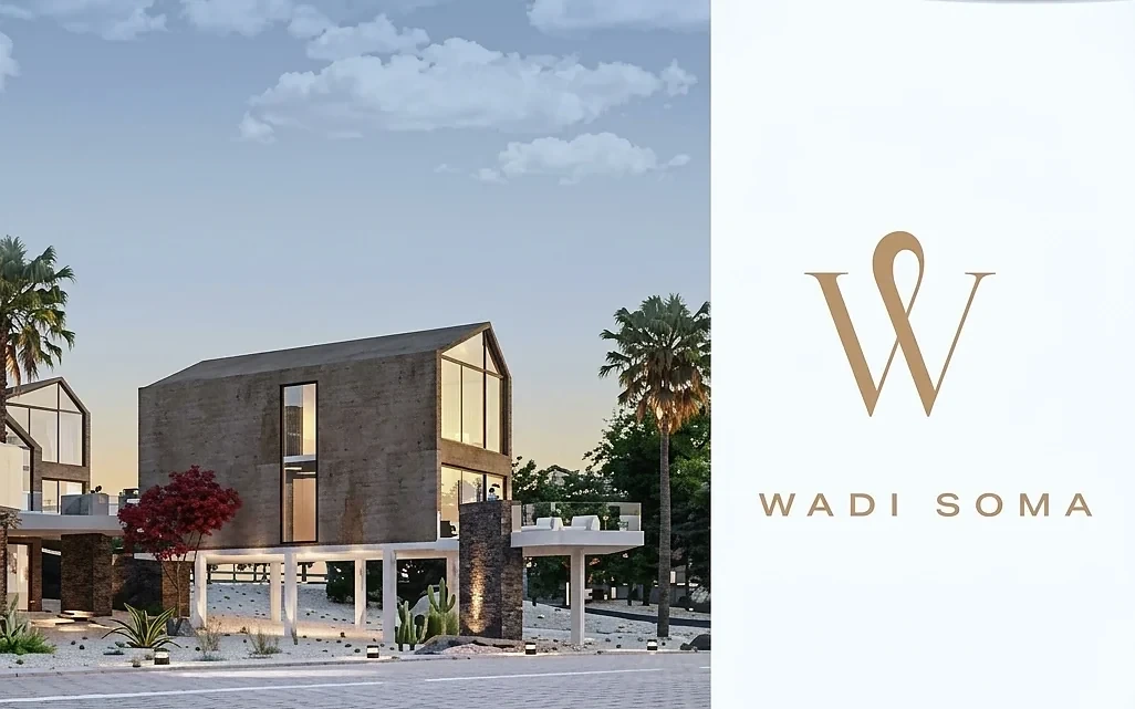 Wadi Soma — a gable-roofed villa in board-marked concrete with full-height glazing, raised on white columns, beside the entrance pylon carrying the Wadi Soma monogram at dusk